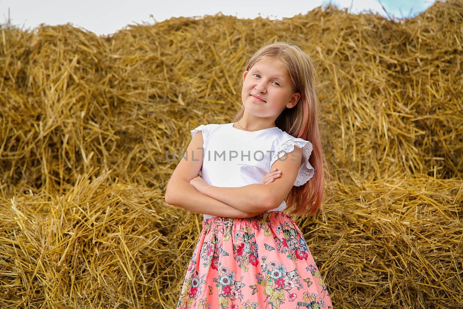 Beautiful girl stands near rolls of straw on a Sunny day