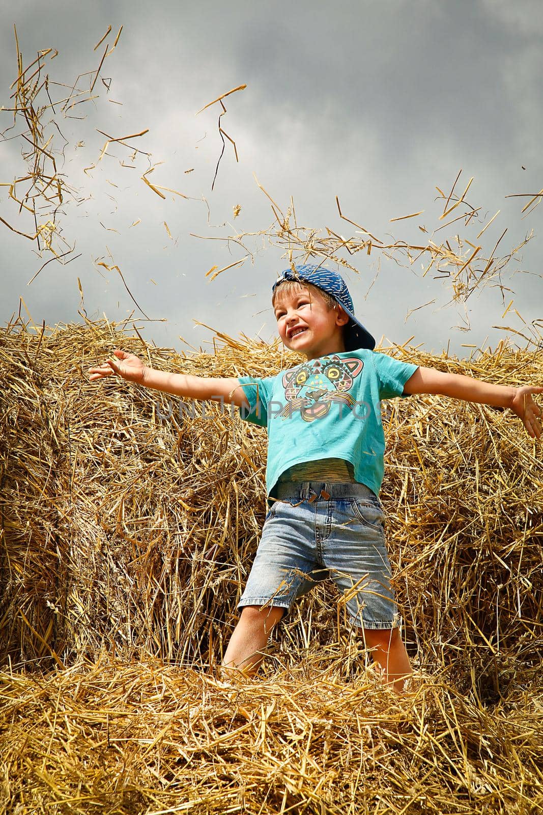 Schoolboy boy jumping and having fun on straw bales on summer day