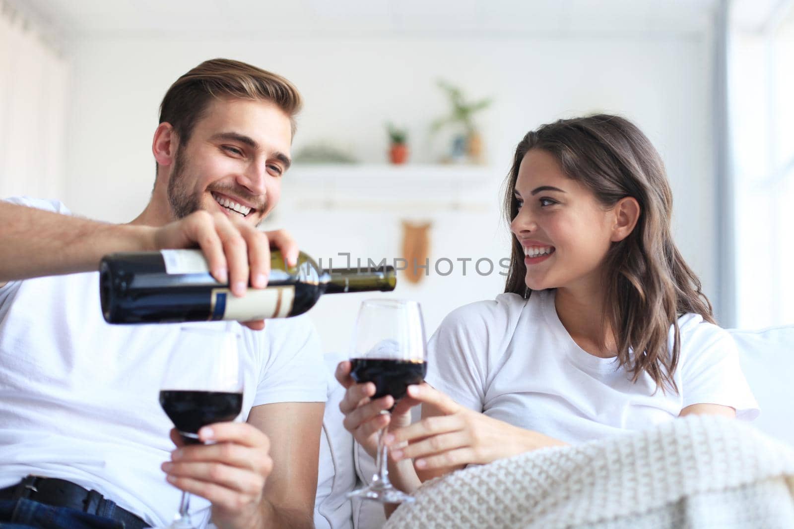 Young loving couple drinking a glass of red wine in their living room. by tsyhun
