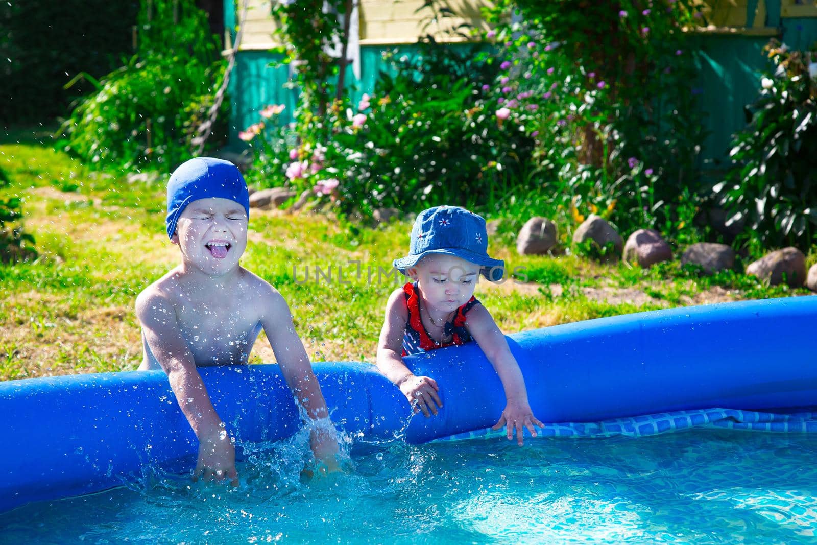 Brother and sister playfully splashing around the blue inflatable pool