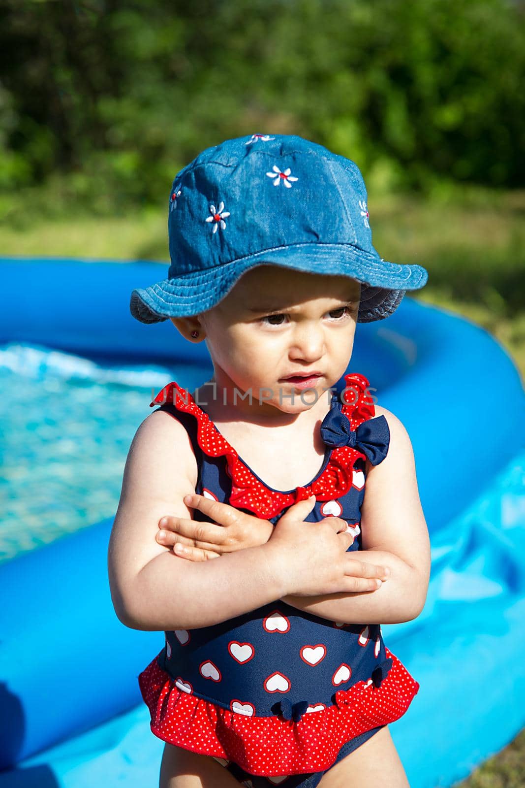 A little girl in Panama and a swimsuit is standing near the inflatable blue pool