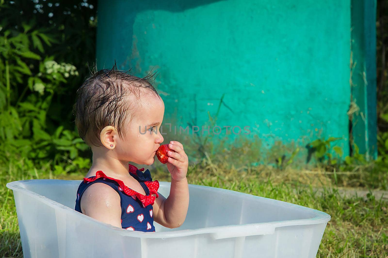 A little girl on a hot day climbed in a swimsuit in the bath and eat strawberries
