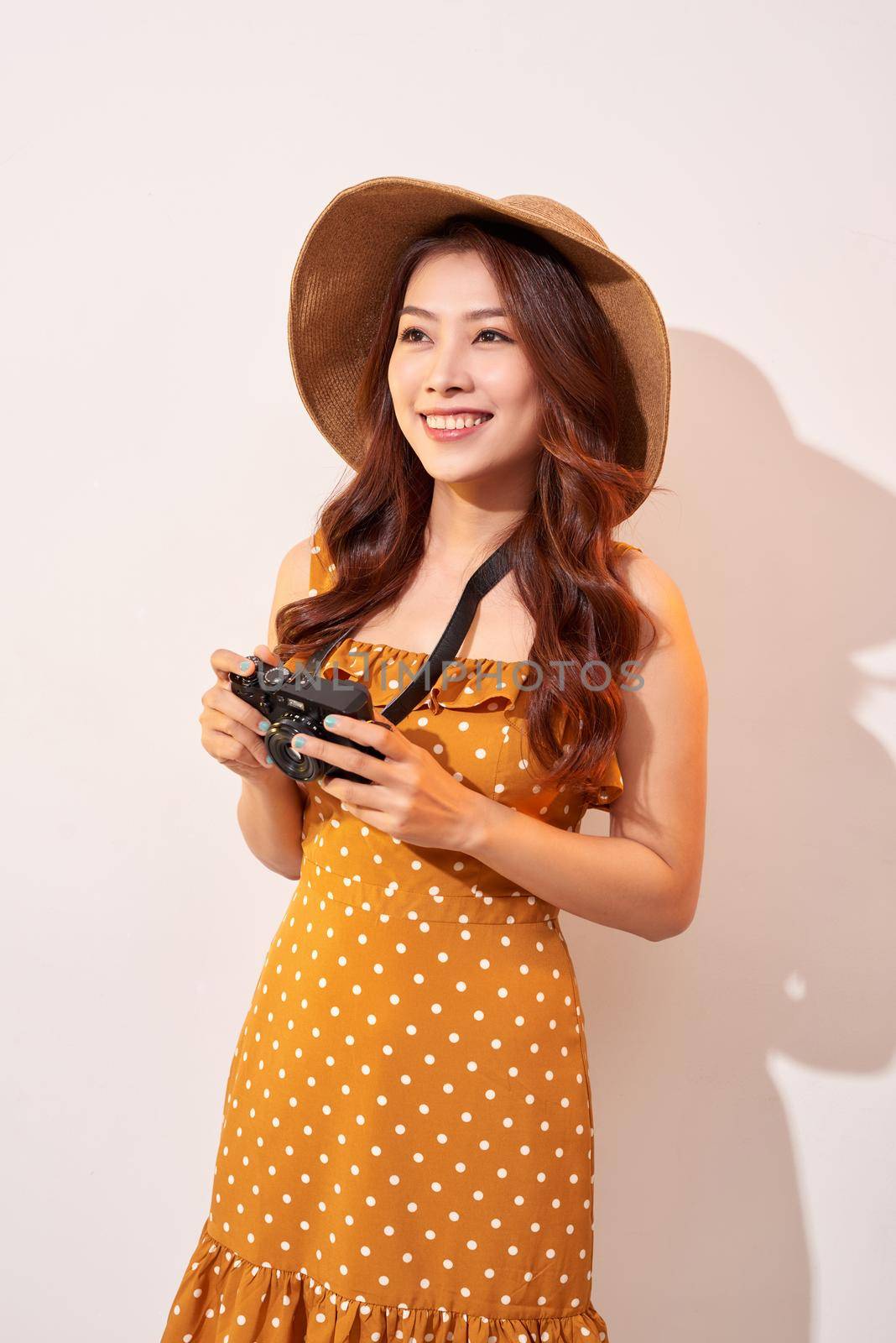 Attractive young woman with a photo camera in her hand on an isolated beige background. The concept travel by makidotvn