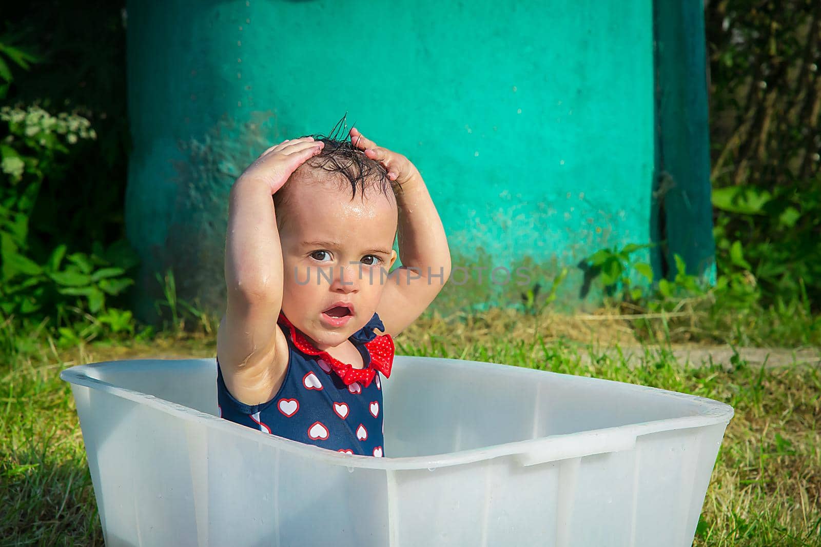 Little girl washes her head sitting in the bath on a hot summer day