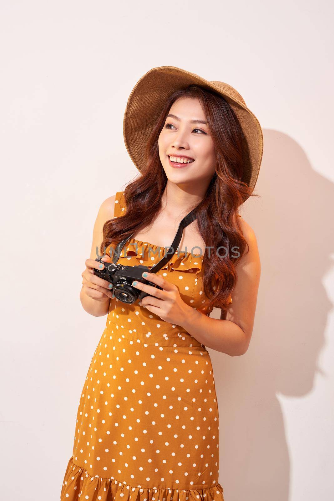 Attractive young woman with a photo camera in her hand on an isolated beige background. The concept travel by makidotvn