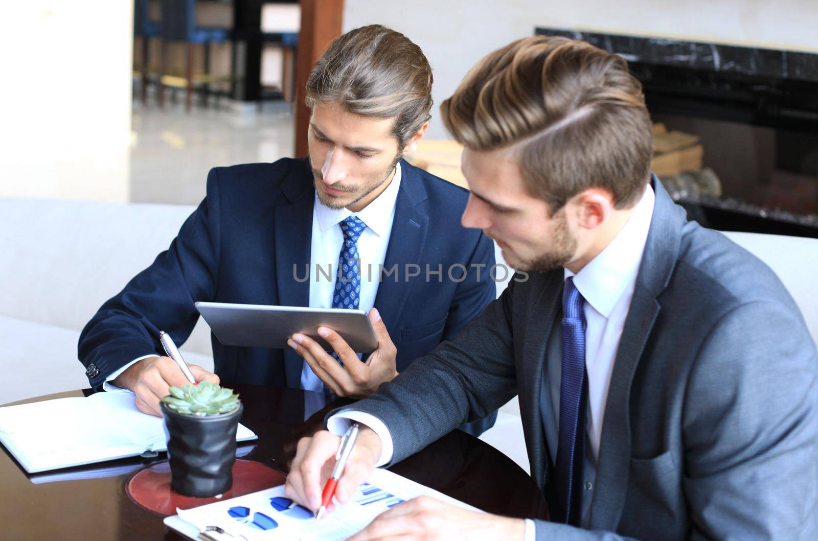 Two young businessmen analyzing financial document at meeting.