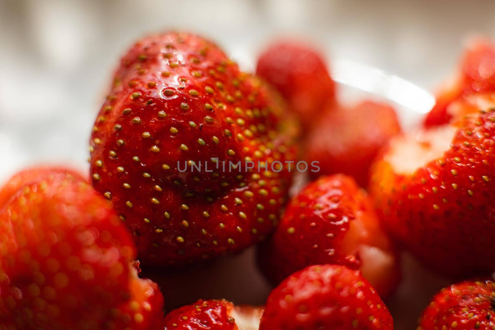 Red strawberry lie in a white ceramic plate on the table under bright sunlight isolated on blur background.