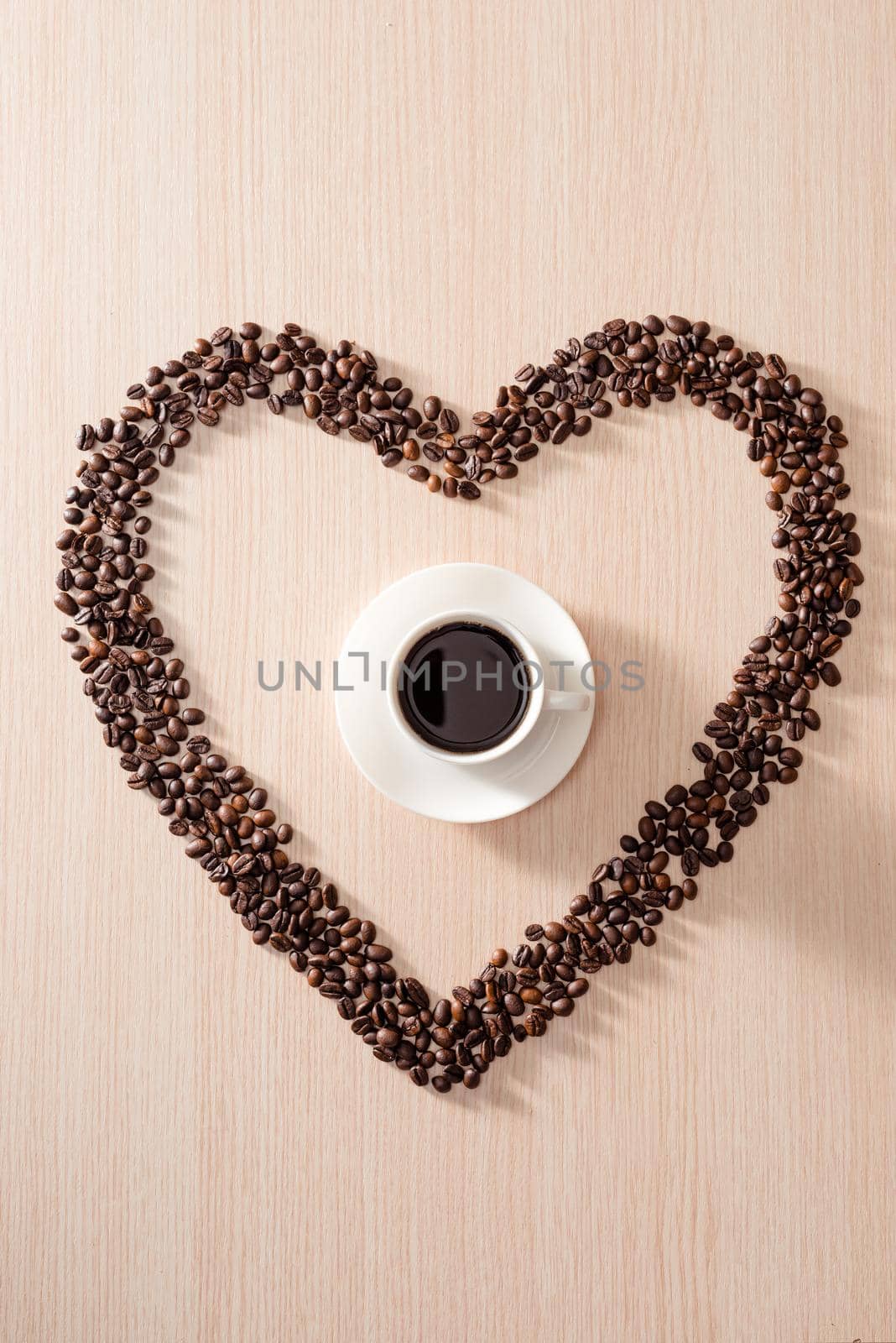 Coffee cup with roasted beans shapes love around on wood background
