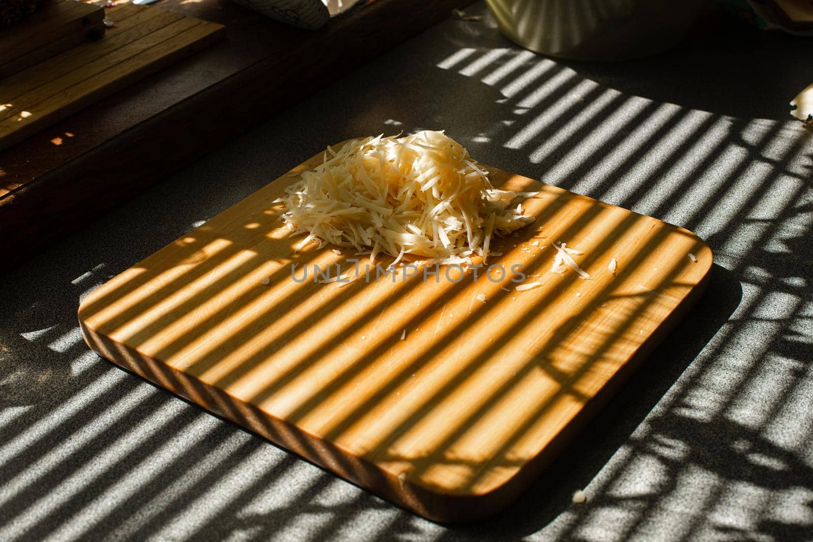 A small pile of grated fresh cheese lies on a wooden board in the kitchen.