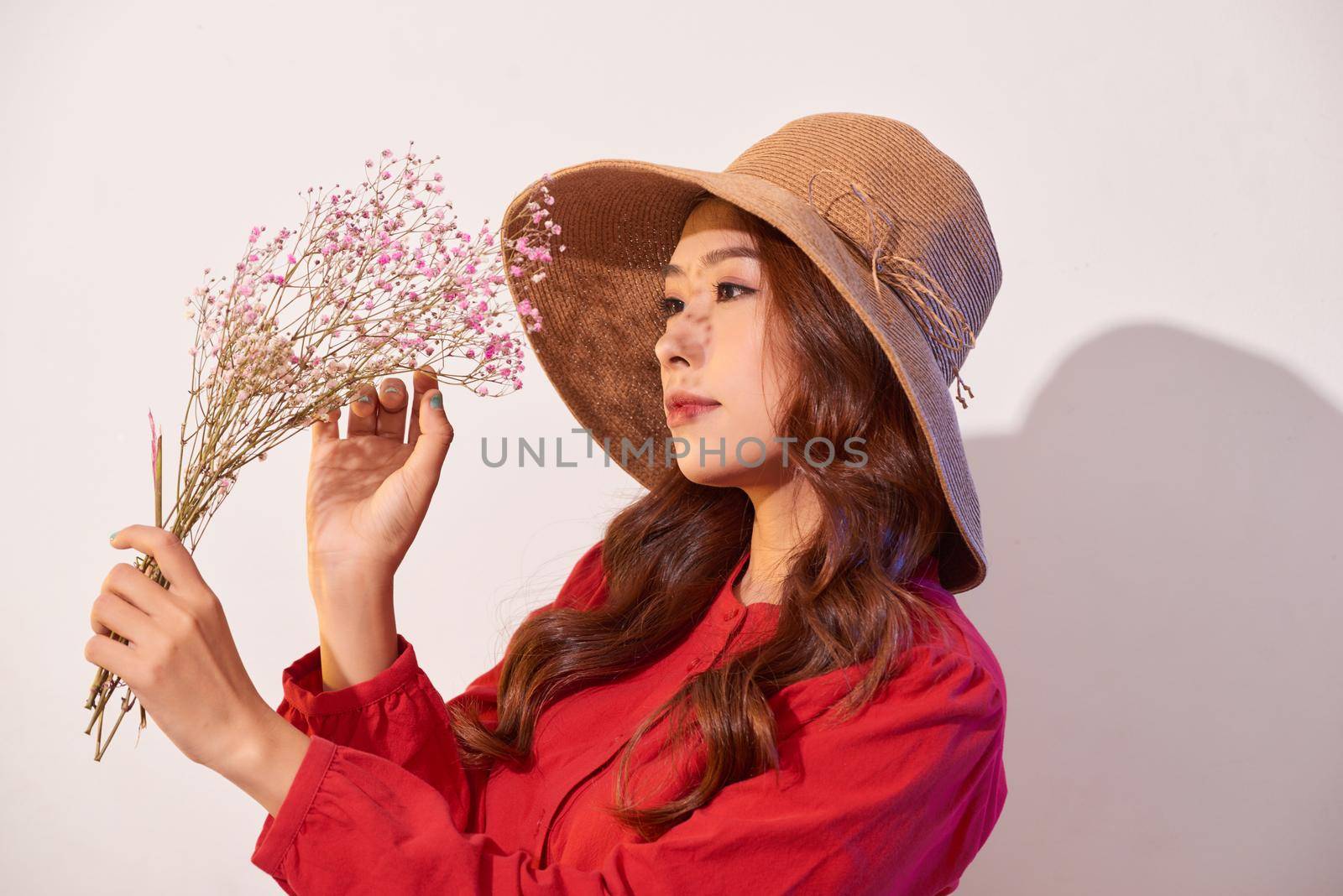 a lovely young woman in summer dress and straw hat posing while holding bouquet flowers