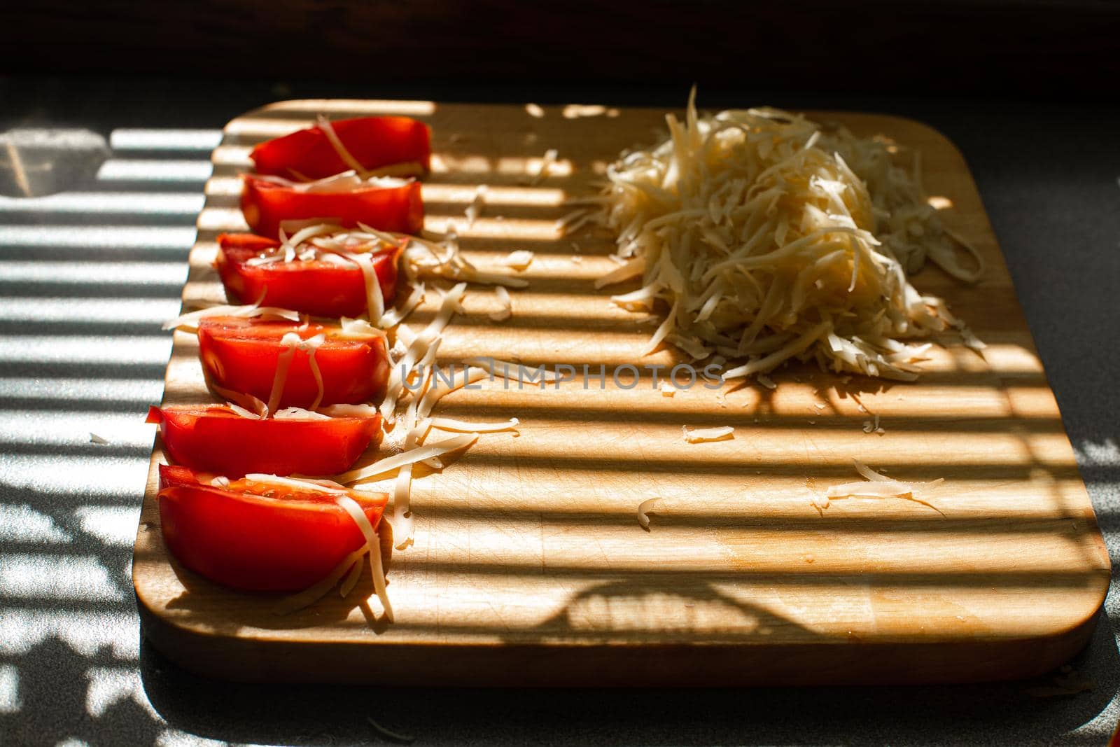 A small pile of grated fresh cheese and red tomatoes lies on a wooden board in the kitchen by StudioLucky