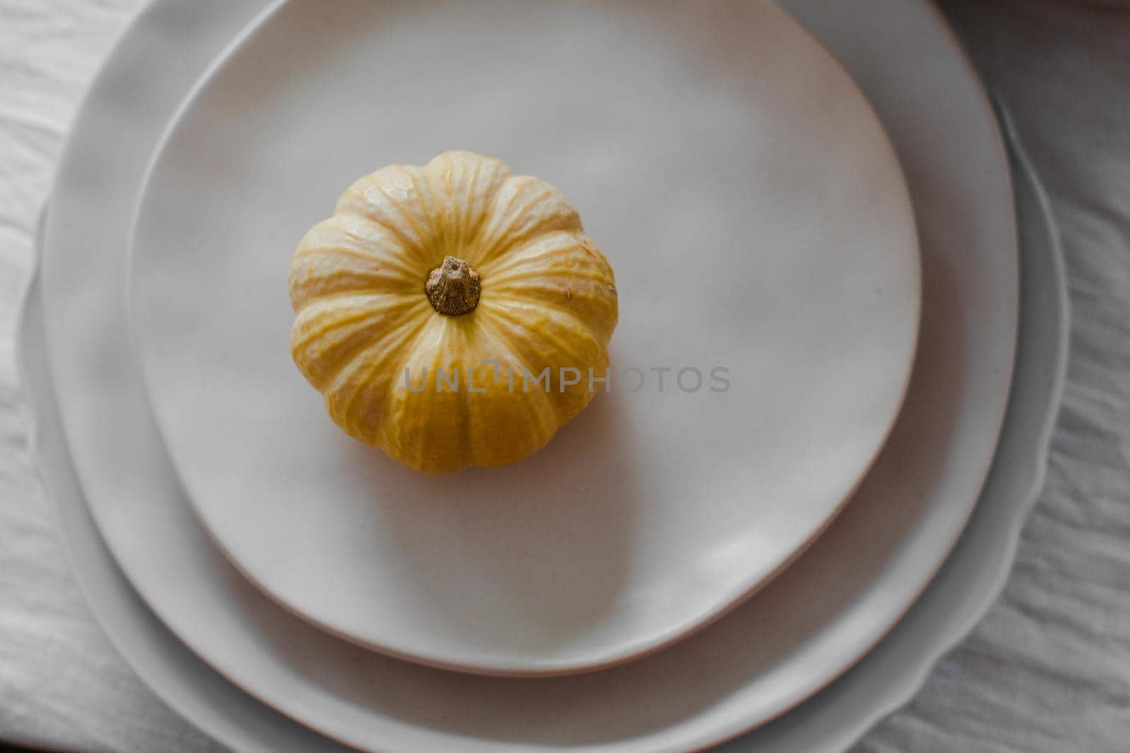 Lovely tiny yellow pumpkin placed on the top of a pile of plates on the table