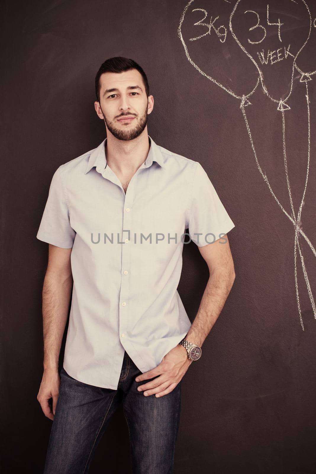 portrait of a happy young stylish man in front of black chalkboard