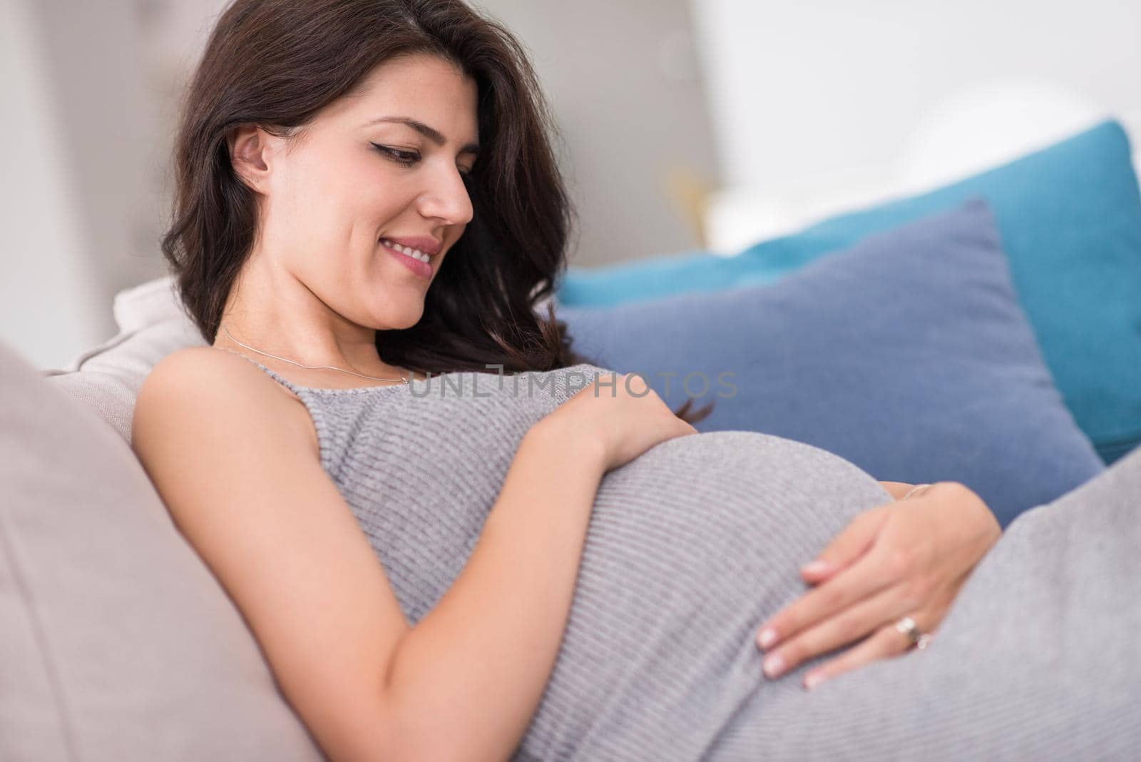 young happy pregnant woman keeping hand on belly while sitting on sofa at home