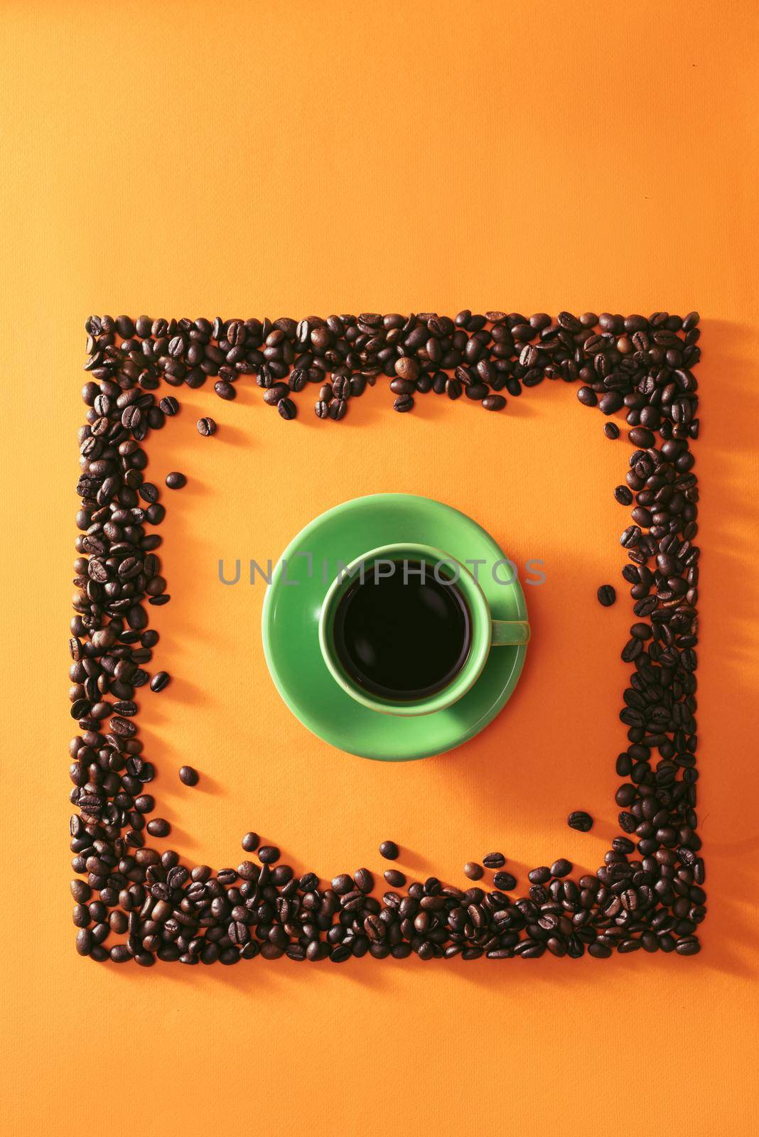 Green cup of coffee in the middle of quare shape coffee beans on orange background by makidotvn