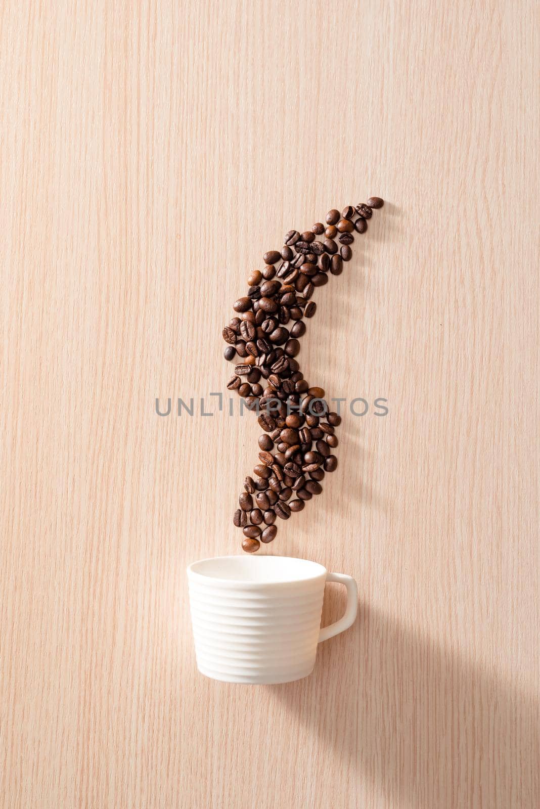 A white cup with smoke shape coffee beans on wooden background