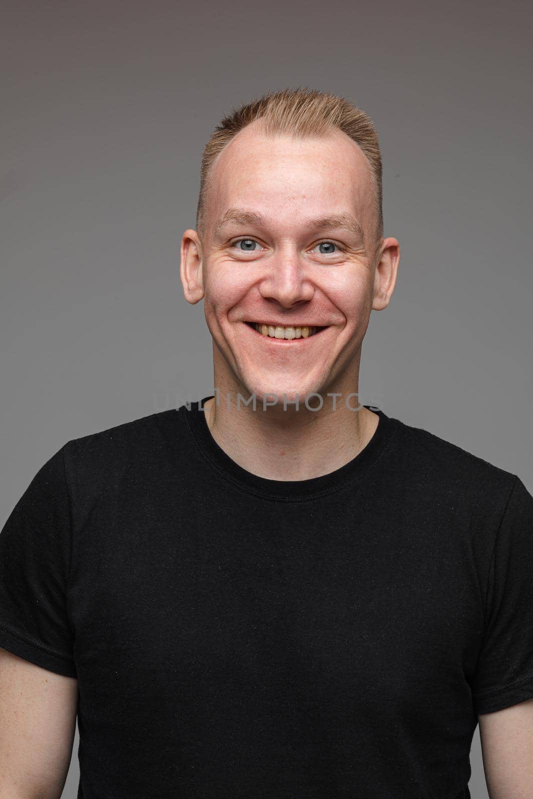 portrait of caucasian man in black t-shirt looks to the camera and smiles isolated on grey background by StudioLucky