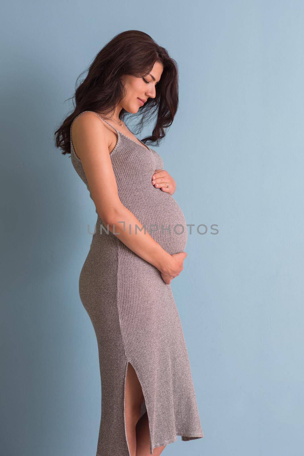 Portrait of happy pregnant woman with hands on belly isolated over blue background