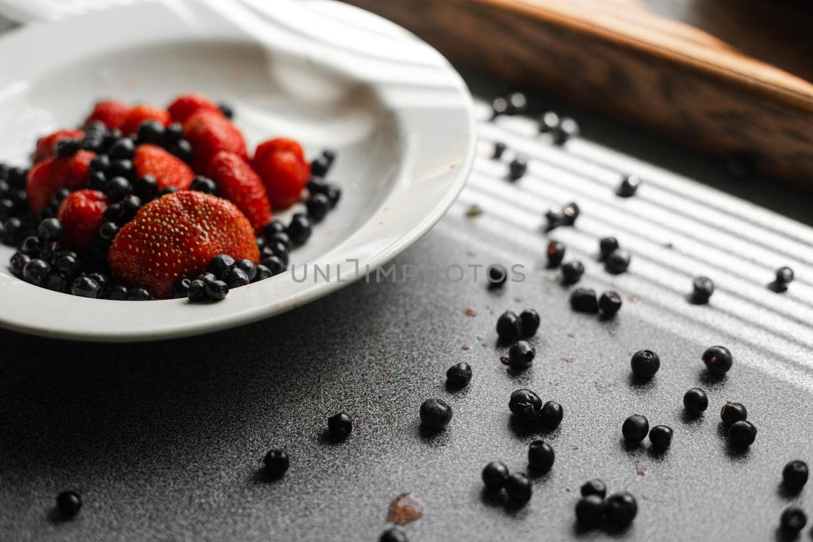 Top view of strawberries and black currants in a white plate near the window. Healthy food concept