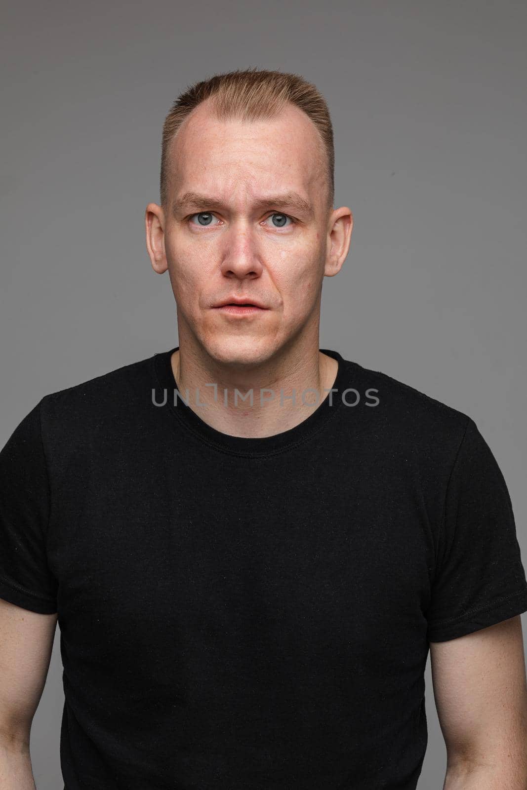 portrait of caucasian man in black t-shirt looks to the camera and smiles isolated on grey background by StudioLucky