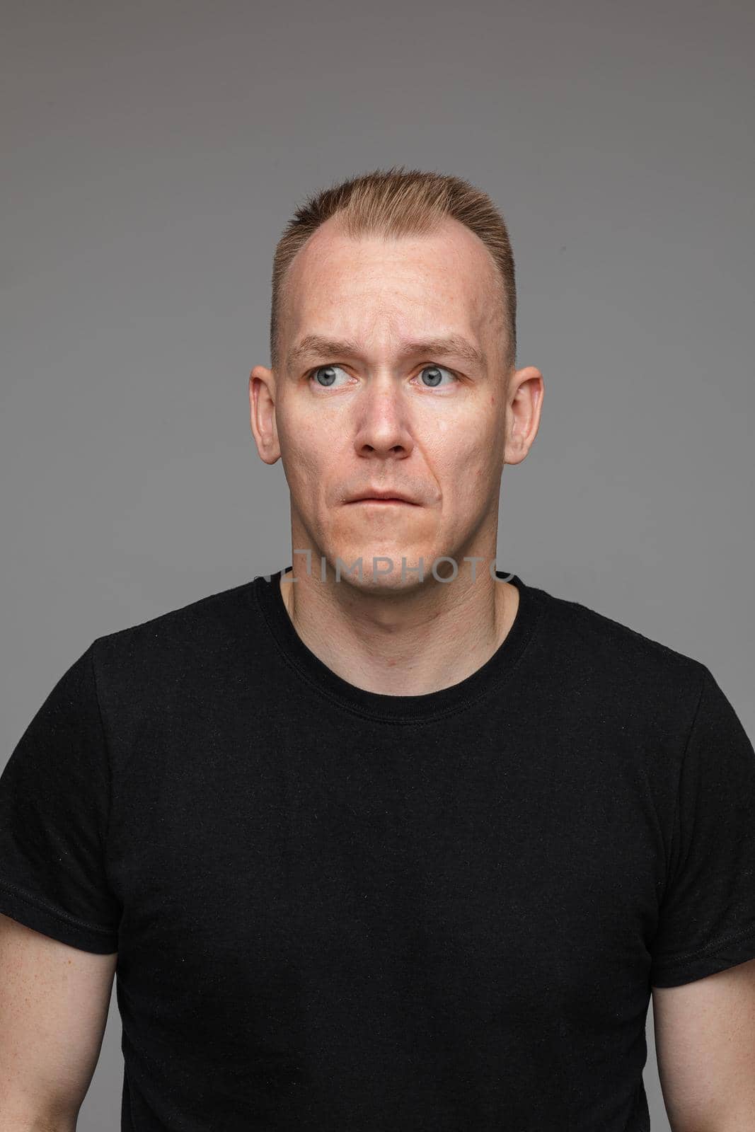 adult caucasian man in black t-shirt and short hair looks aside and thinks