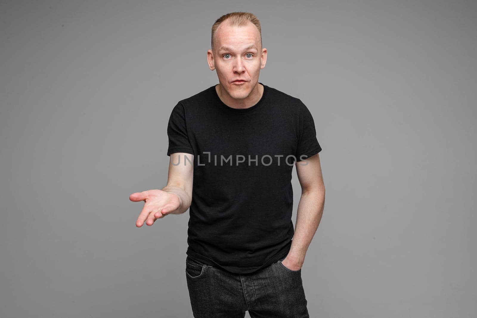 attractive man with short fair hair wearing a black t-shirt and jeans looking at the camera and points his hand to copyspace by StudioLucky