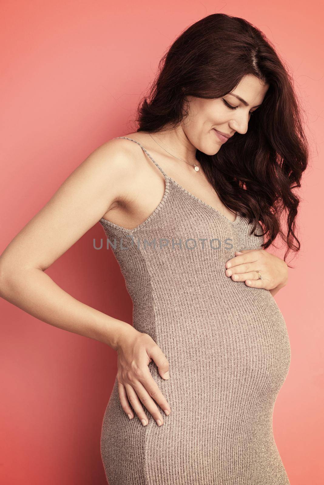 Portrait of happy pregnant woman with hands on belly isolated over red background