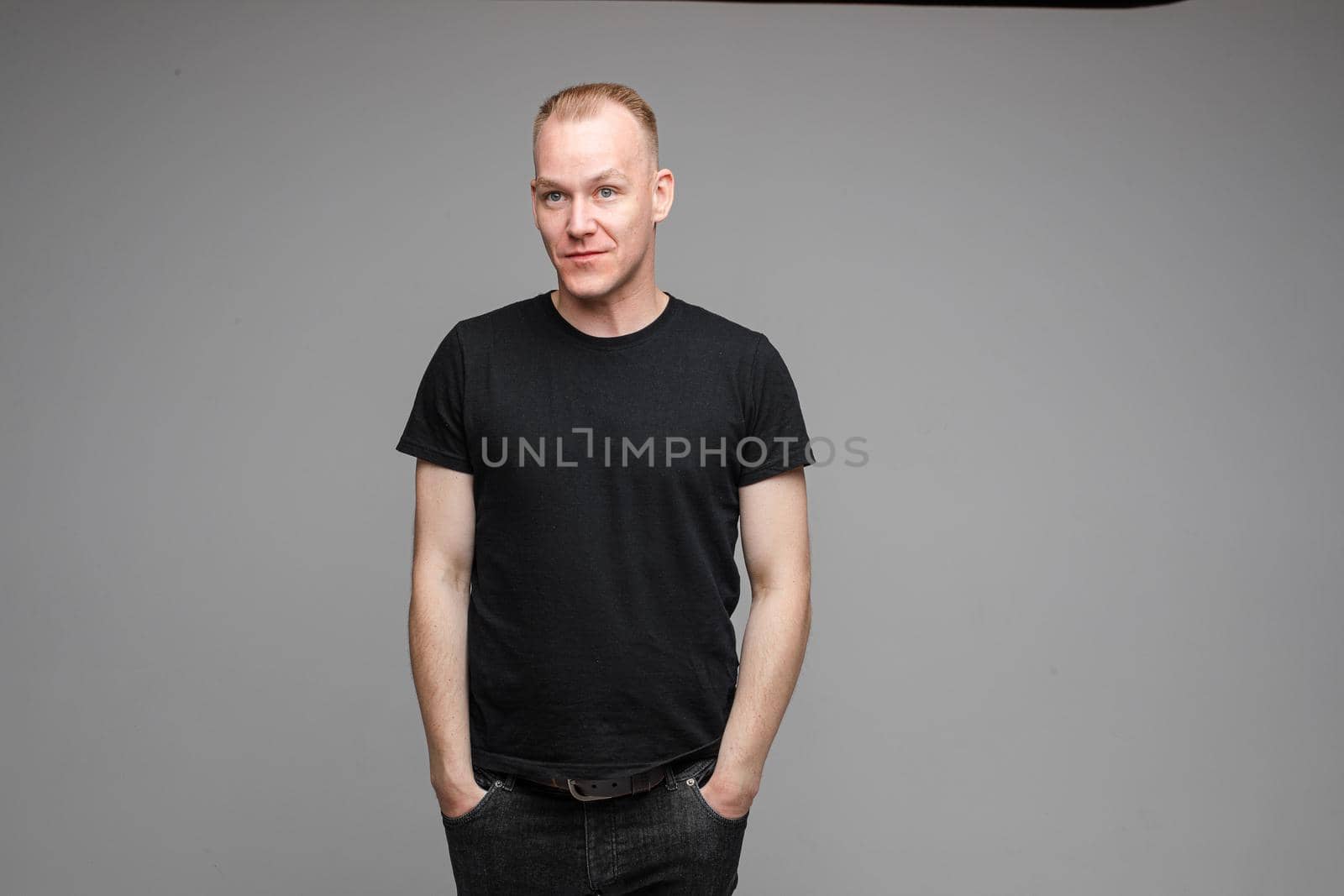 picture of attractive male wearing a black t-shirt and jeans poseing for the camera with hands in pockets on grey background