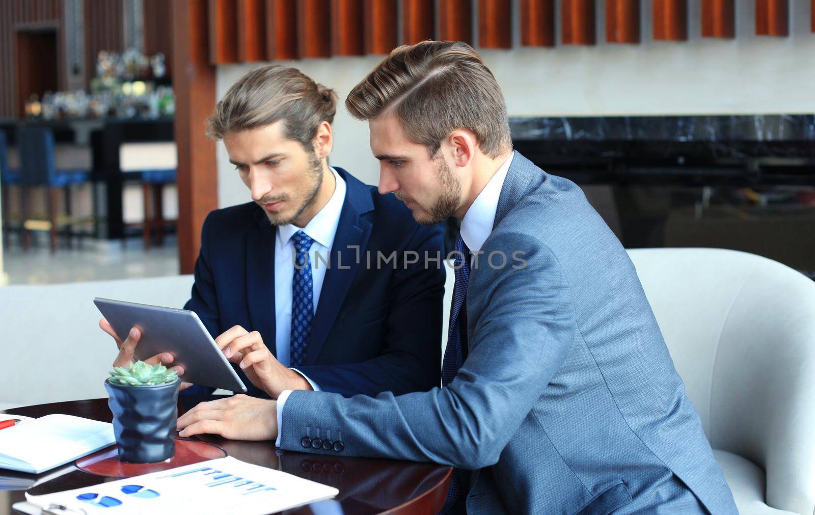 Two young businessmen using touchpad at meeting. by tsyhun