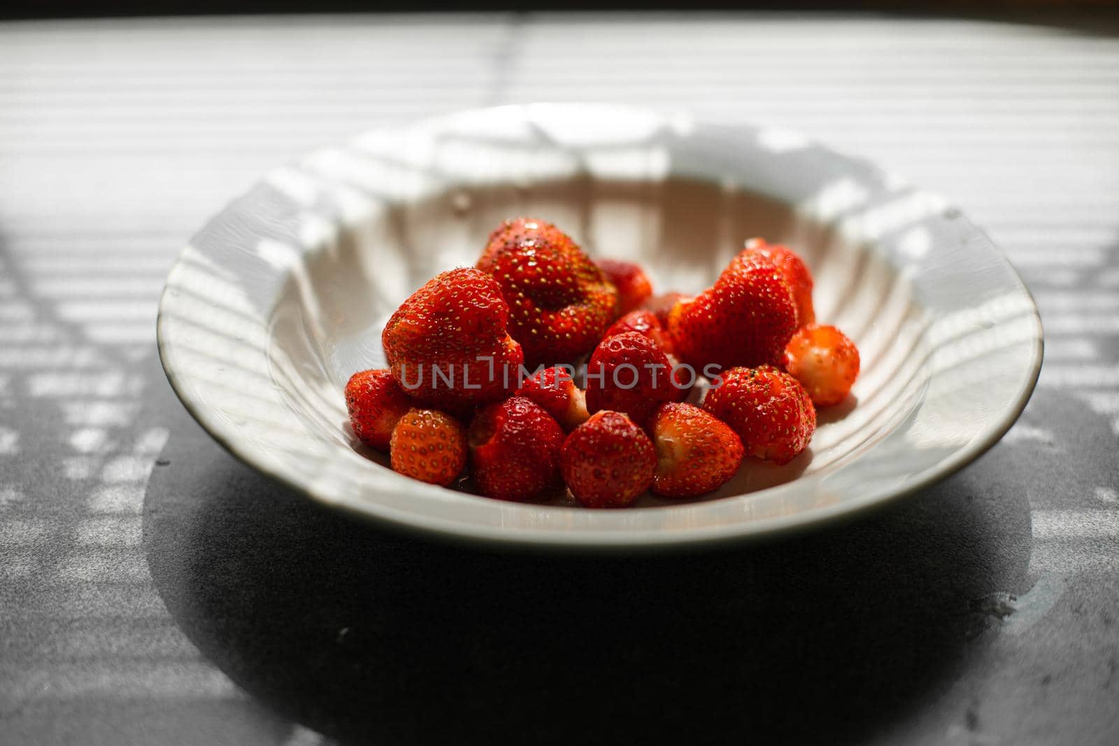 Top view of washed and cleaned ripe strawberries in a simple white bowl on the table indoors. Healthy food concept