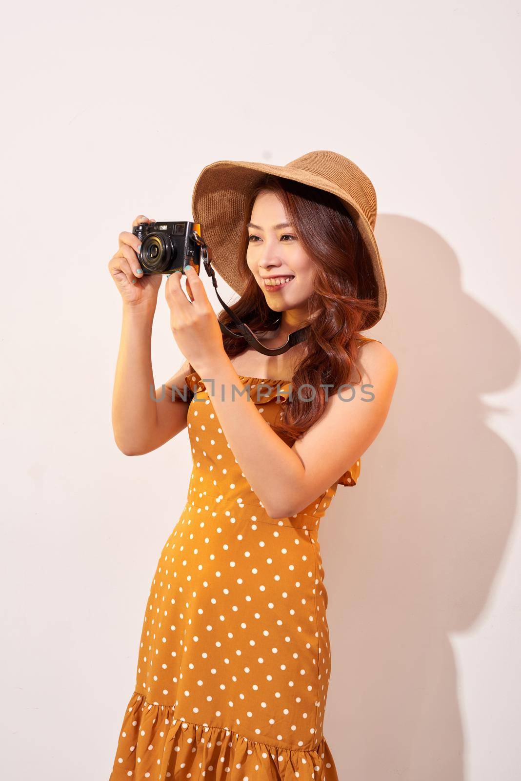 Attractive young woman with a photo camera in her hand on an isolated beige background. The concept travel by makidotvn