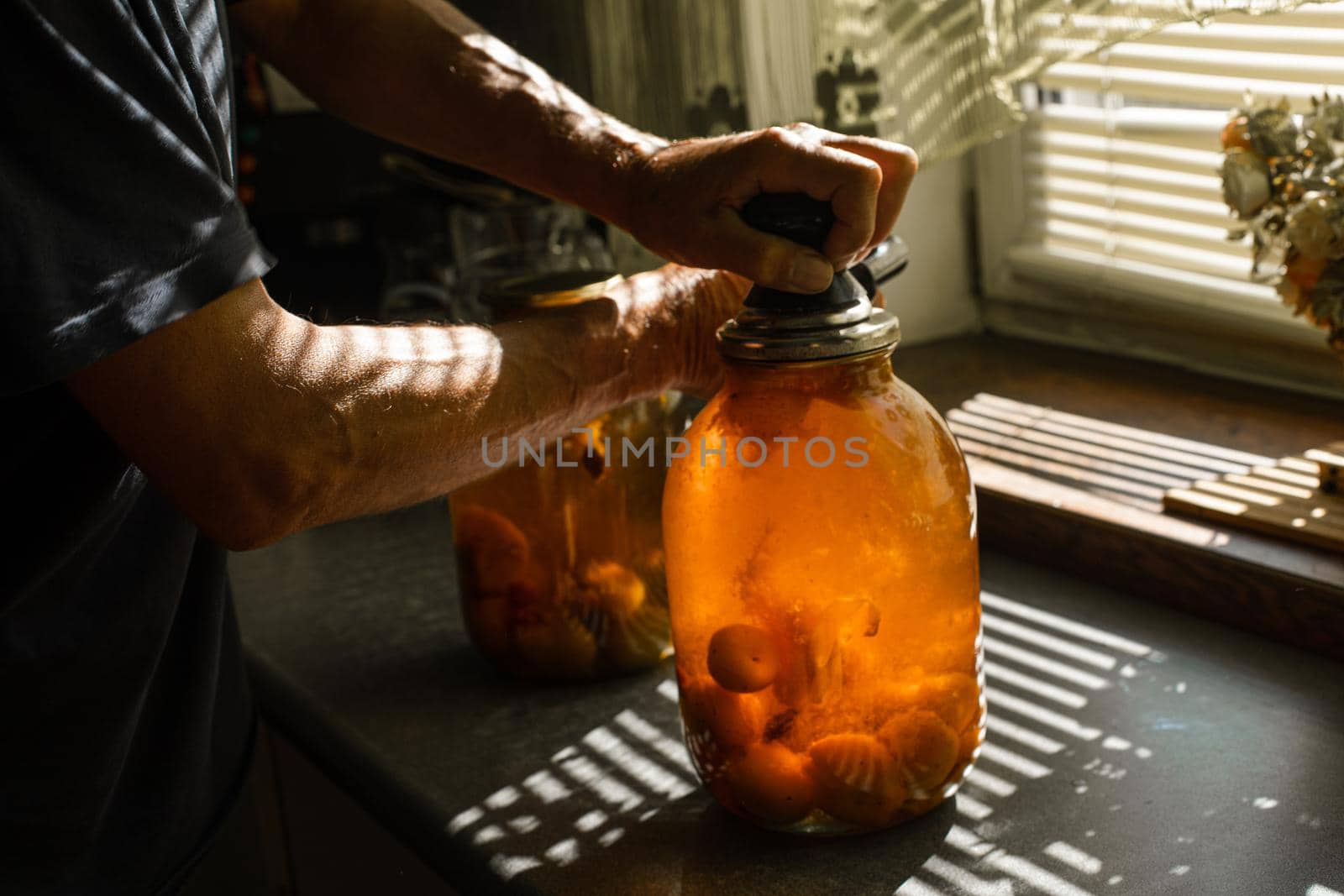 A woman rolls a compote in a large jar under the sun in summer at home in the village.