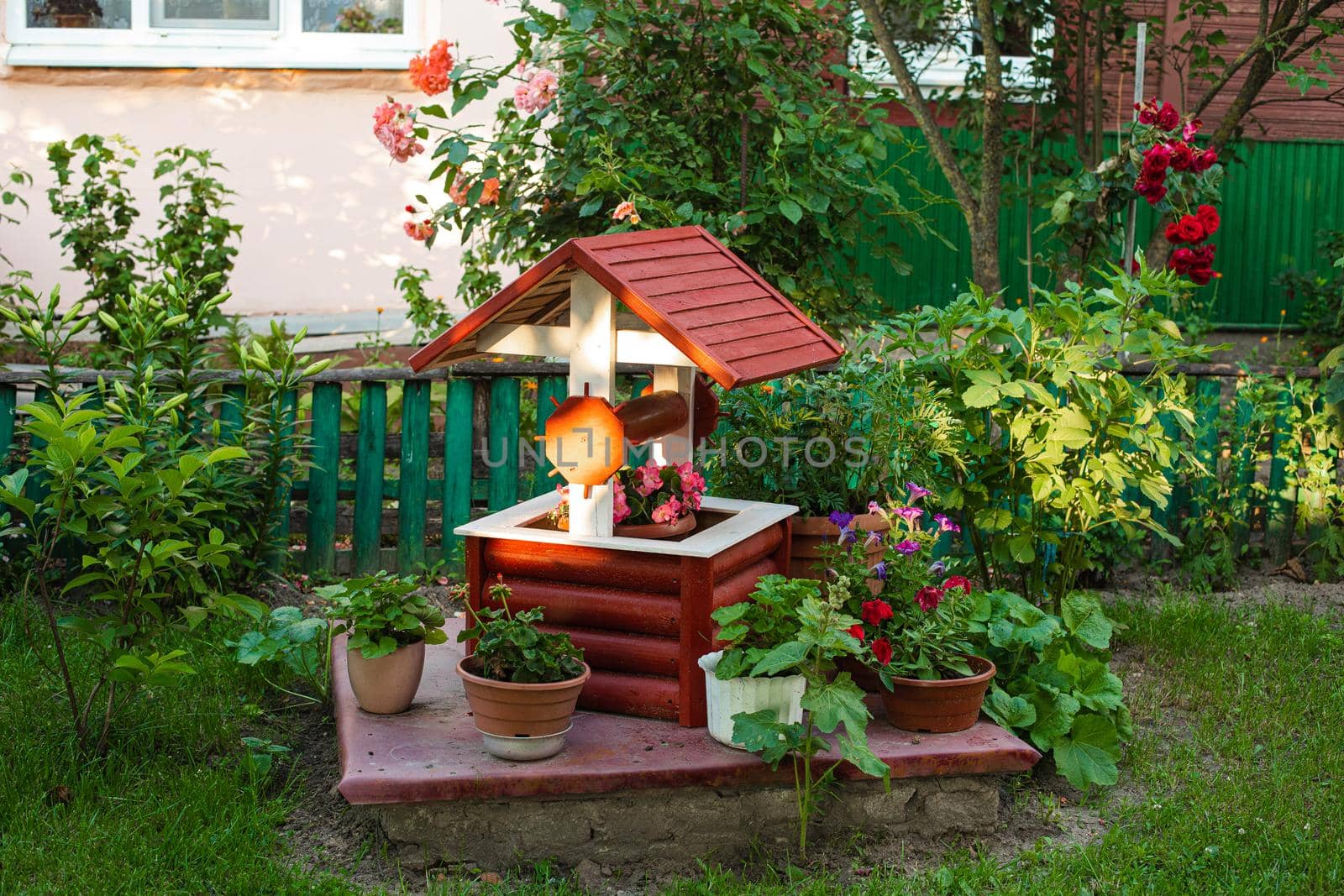 Stock photo of a small garden in the backyard. Fake well with potted flowers. Rustic backyard in countryside or village.