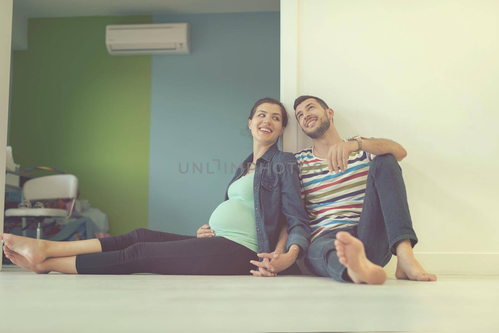 happy pregnant couple holding their hands while sitting on the floor at home