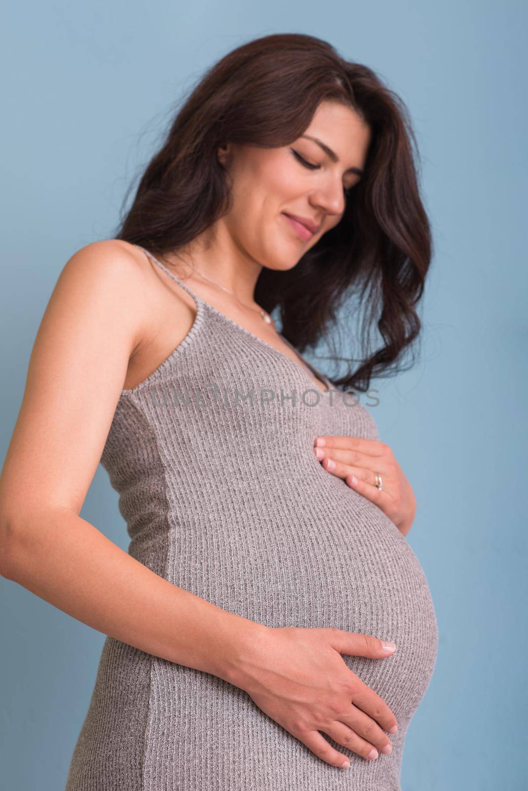 Portrait of happy pregnant woman with hands on belly isolated over blue background