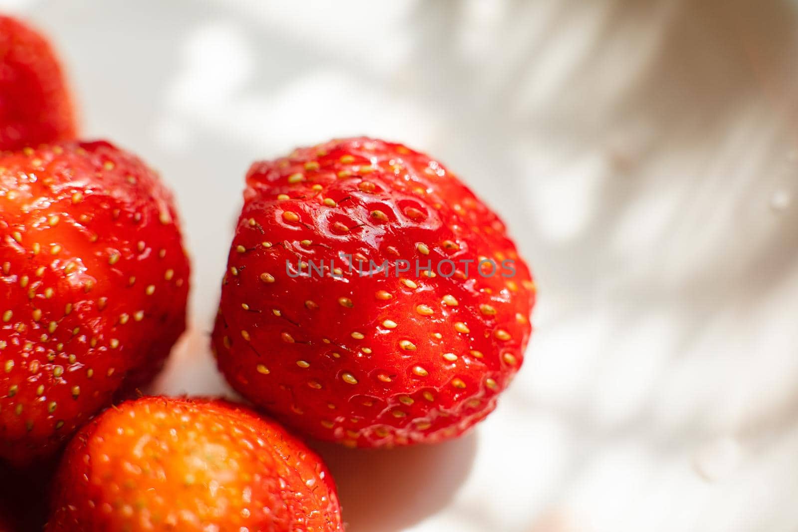Macro stock photo of large organic sweet strawberries in sunlight. Strawberry texture in close-up. Seeds and dirt.