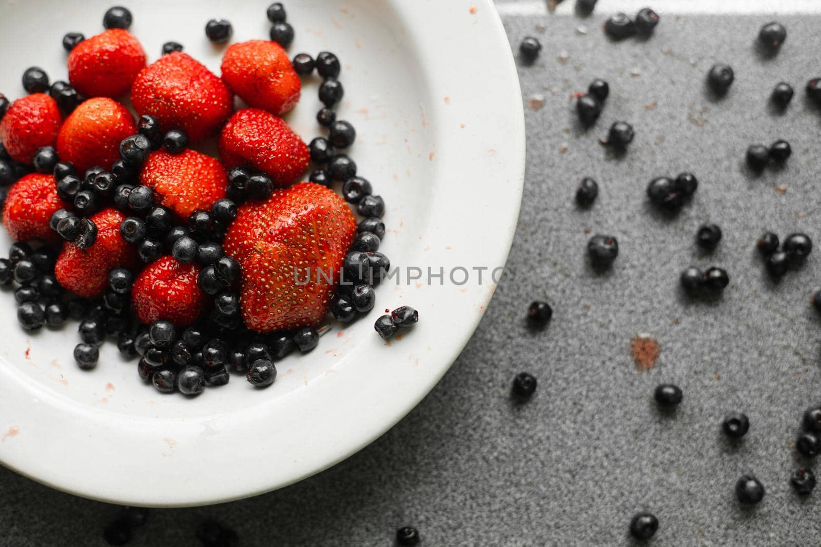 Many juicy fresh ripe red berries and blackberries lie in a white ceramic plate on the table by StudioLucky