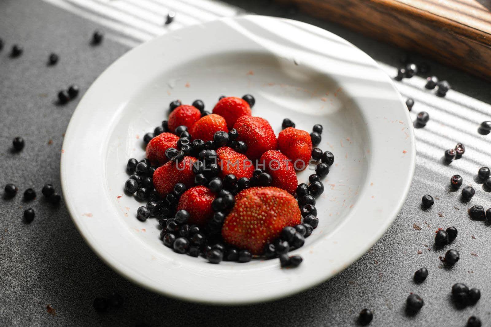 Top view of strawberries and black currants in a white plate near the window. Healthy food concept