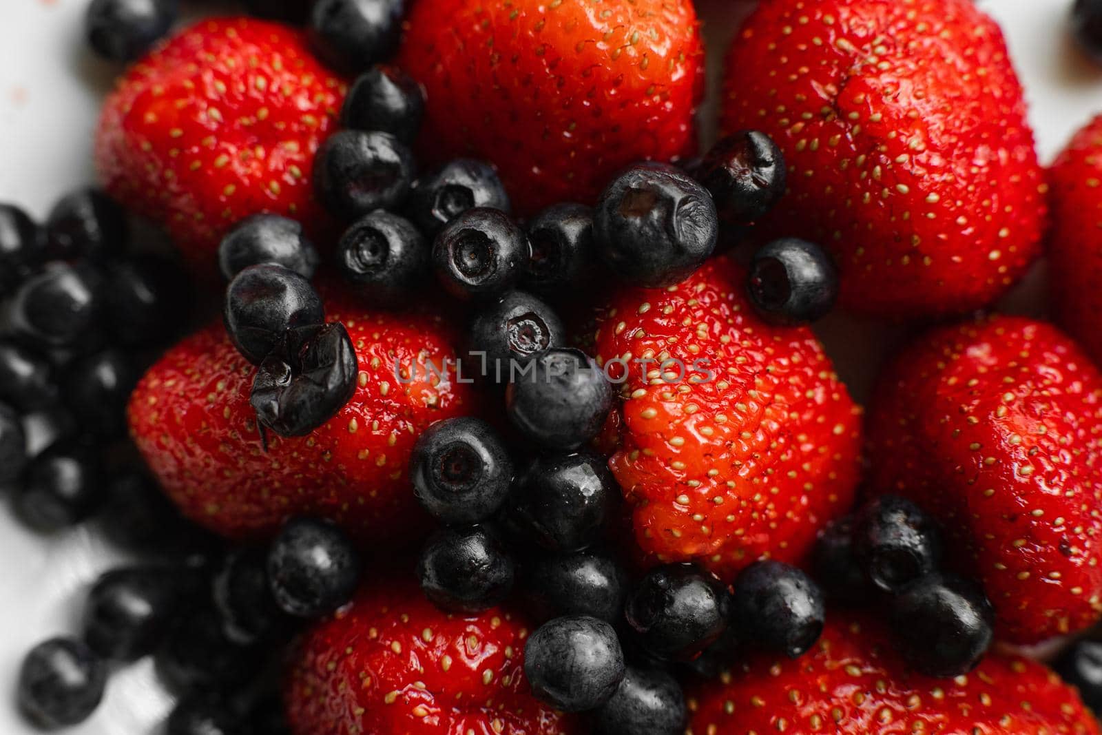 Top view of berries fresh colorful assortment, strawberries and black currants on white plate. Healthy food concept