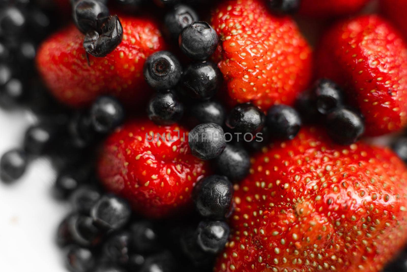 Top view of berries fresh colorful assortment, strawberries and black currants on white plate. Healthy food concept