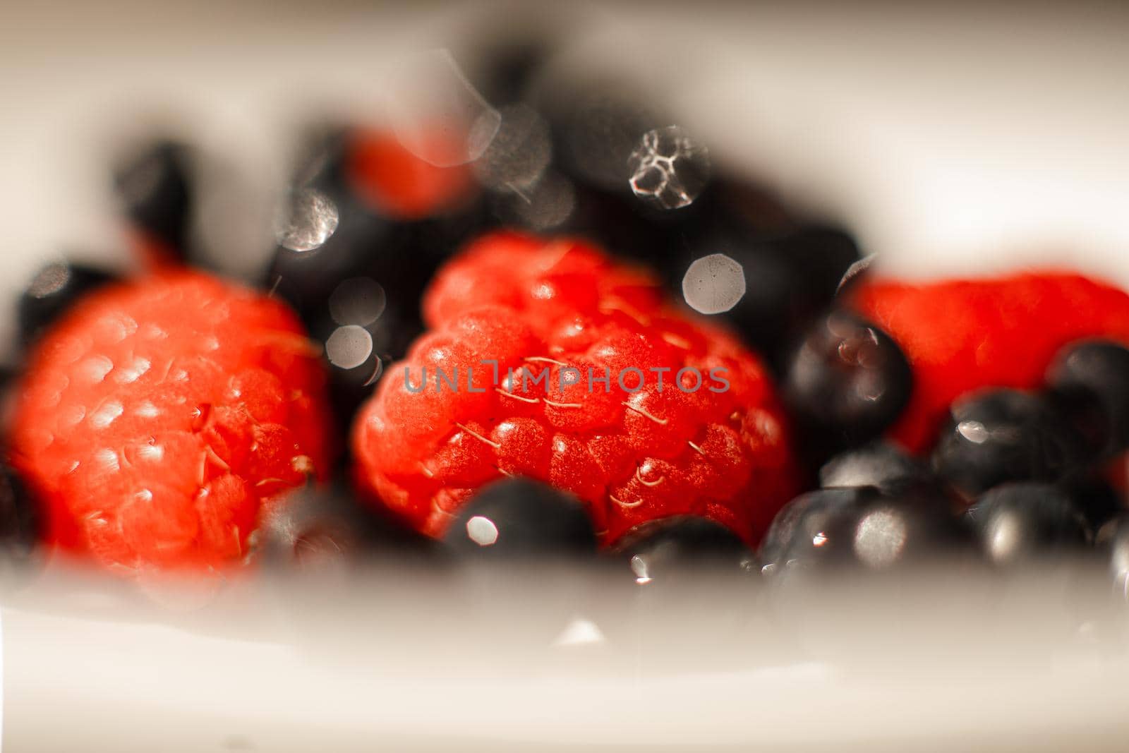 Many juicy fresh ripe red strawberry berries lie in a white ceramic plate on the table under bright sunlight by StudioLucky