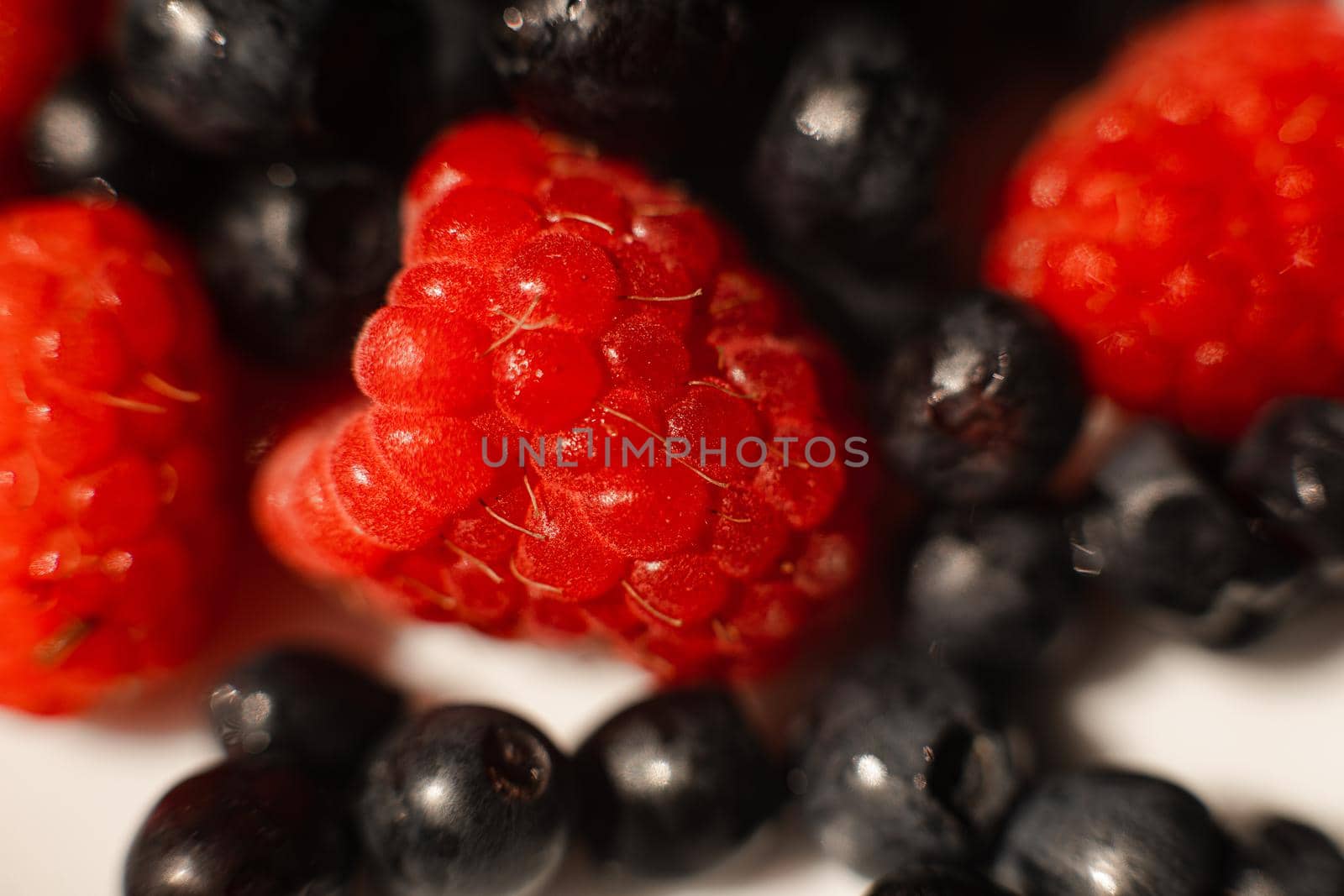 Many juicy fresh ripe red strawberry berries lie in a white ceramic plate on the table under bright sunlight by StudioLucky