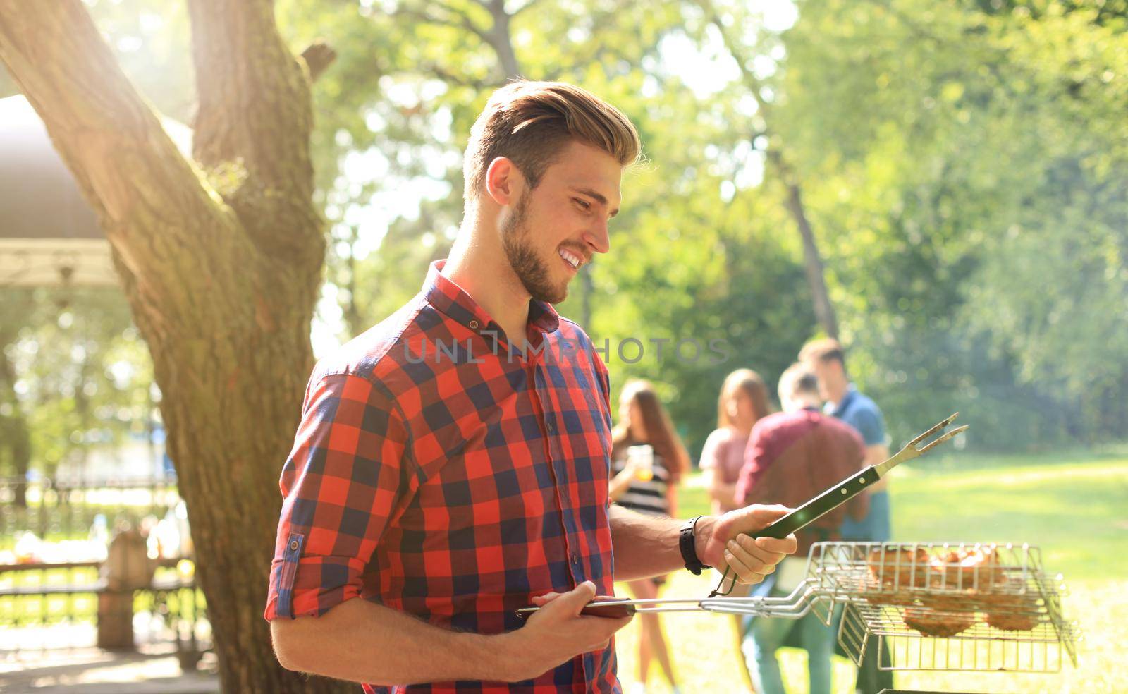 Handsome happy male preparing barbecue outdoors for friends.