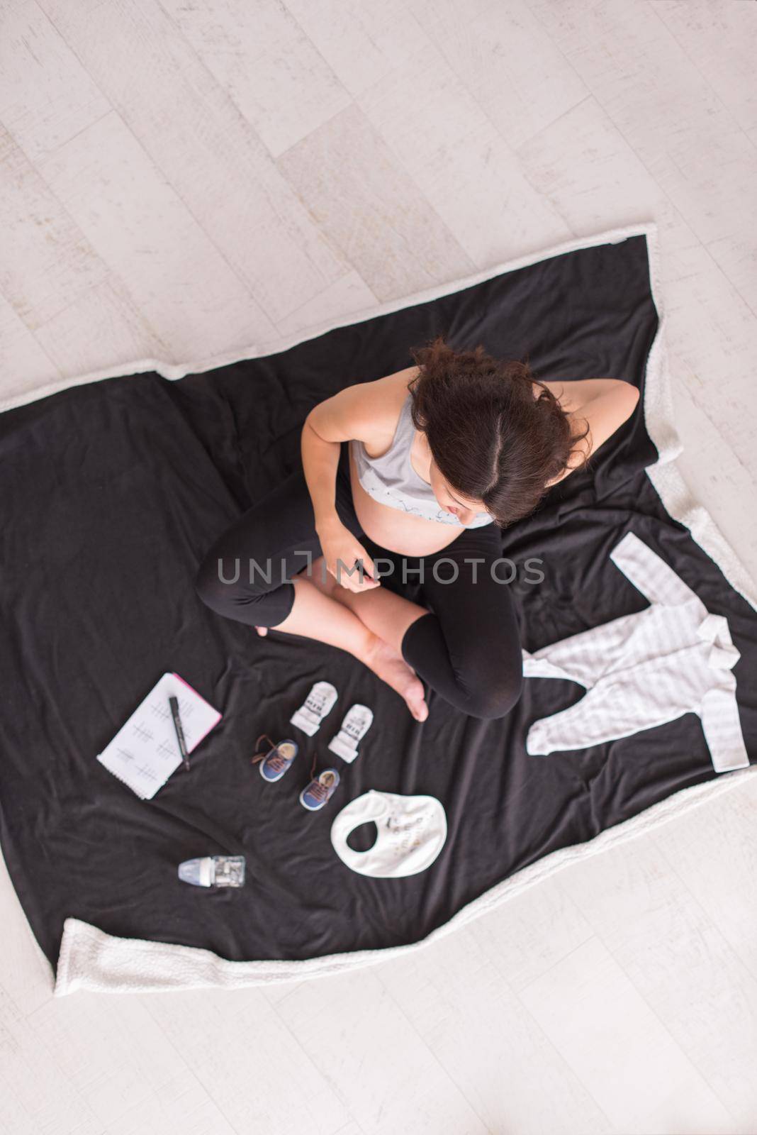 a pregnant woman at home on the floor checking list of baby clothes preparing for going to maternity hospital top view.Pregnancy, birth concept