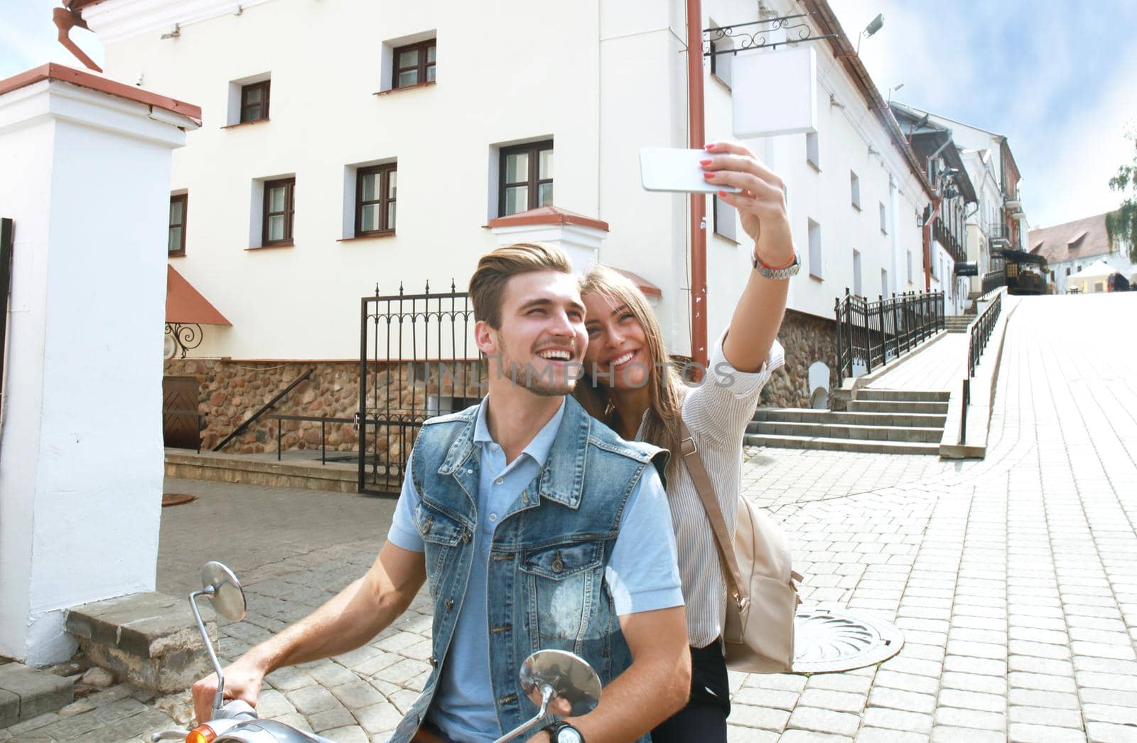 Happy couple on scooter making selfie photo on smartphone outdoors