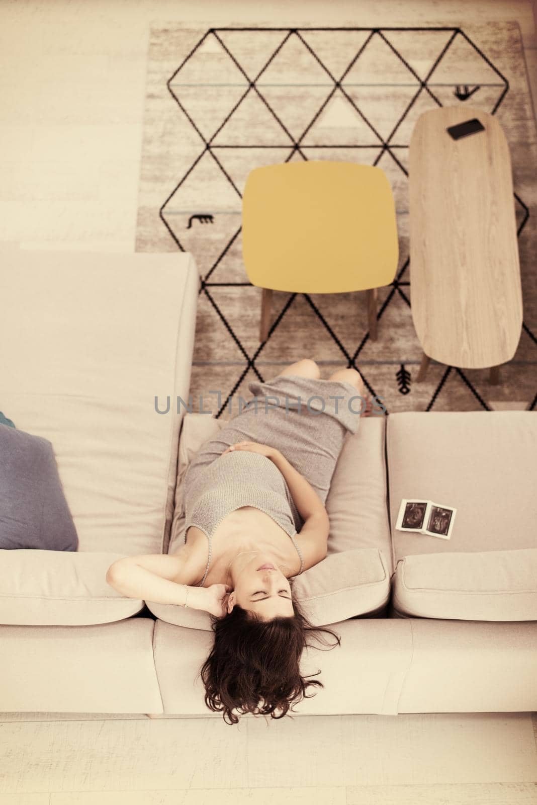 top view of a young pregnant woman looking baby's ultrasound photo while relaxing on sofa at home