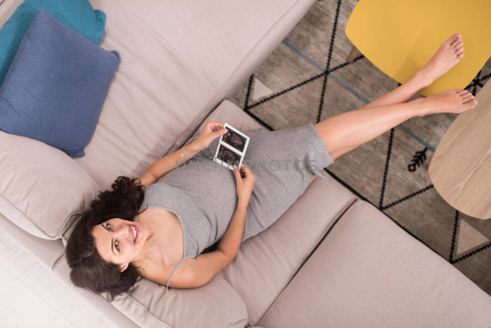 top view of a young pregnant woman looking baby's ultrasound photo while relaxing on sofa at home