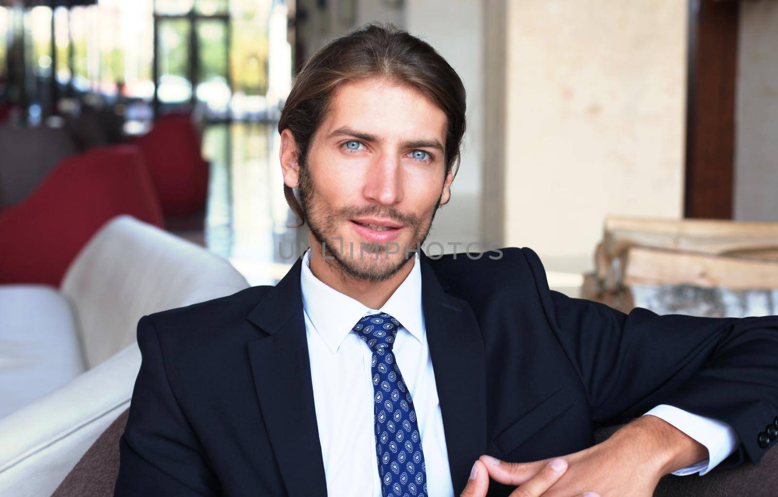 Portrait of happy young businessman sitting on sofa in hotel lobby