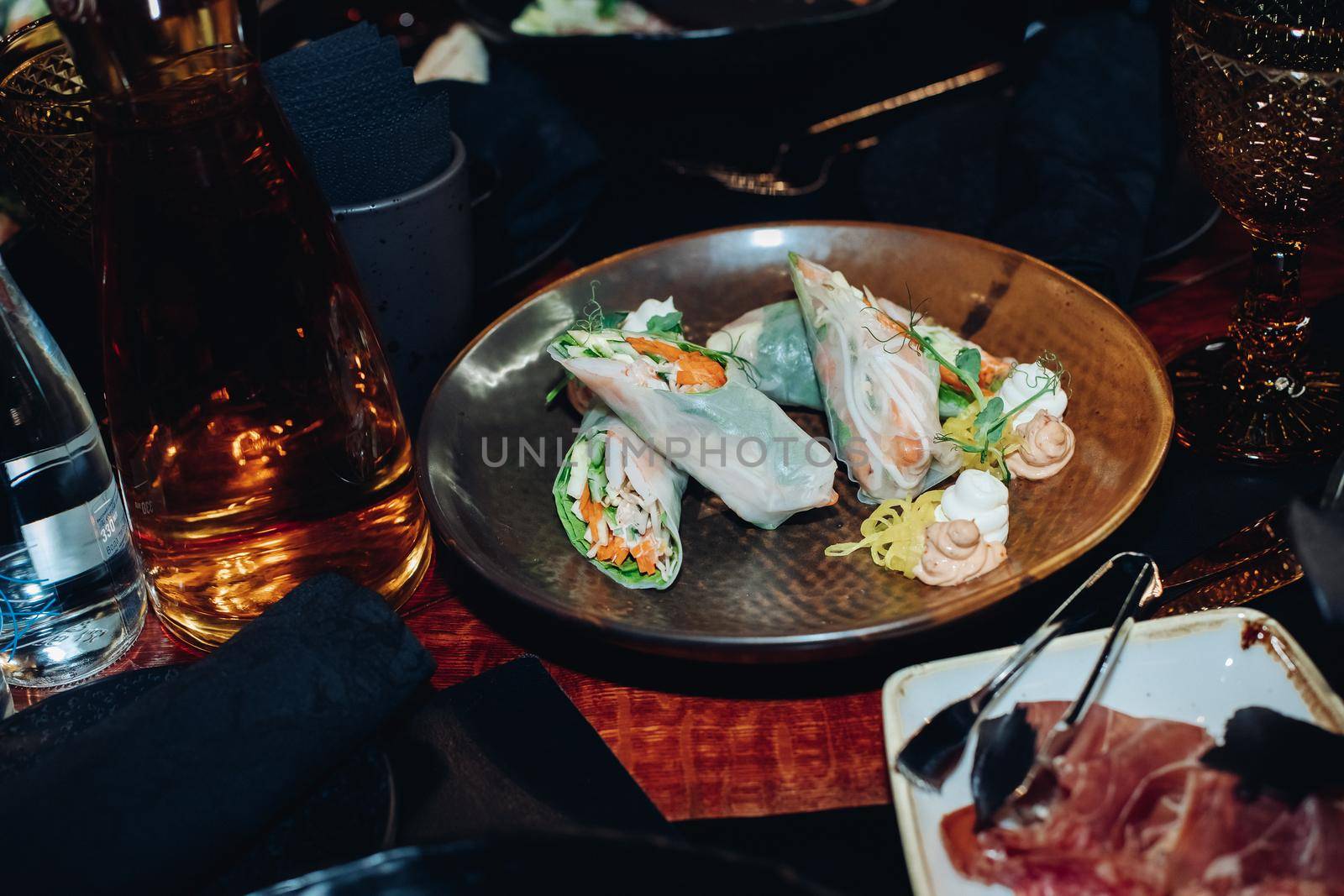 Stock photo of delicious fresh rolls with raw vegetables and noodles served on plate with sauces and greens.