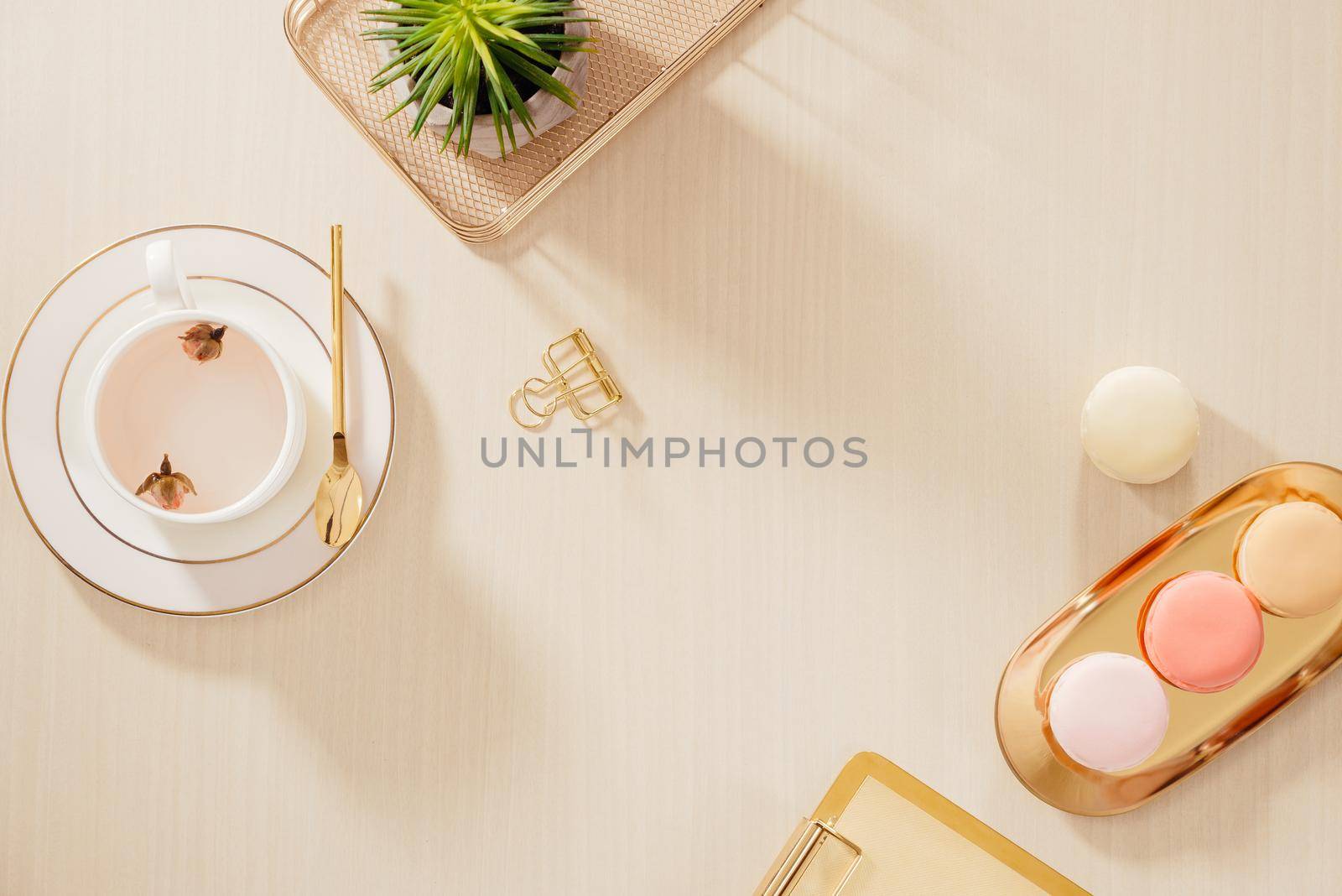 Modern gold stylized home office desk with folder, macaroons, coffee mug on beige background. Flat lay, top view lifestyle concept.`